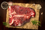Raw US Angus T-bone steak on kraft paper with rosemary and garlic